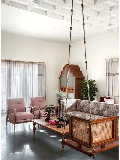 Behind the courtyard is the living room, a modest yet elegant space featuring the quintessential Indian swing. All-teak furniture provides warmth, a patterned fabric on the sofa adds ethnic appeal, and the coffered ceiling brings the space together into a cozy haven.