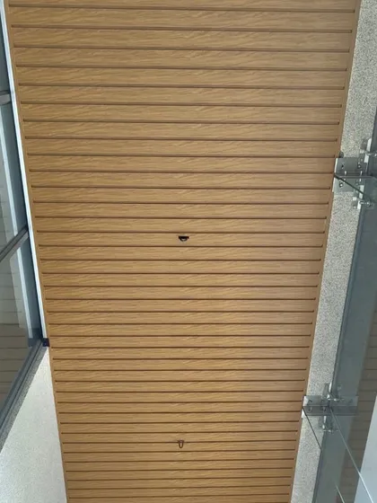 A wide view of a metal ceiling with a light oak finish installed in a covered outdoor walkway. It seamlessly integrates with the modern architecture while adding a touch of natural warmth.