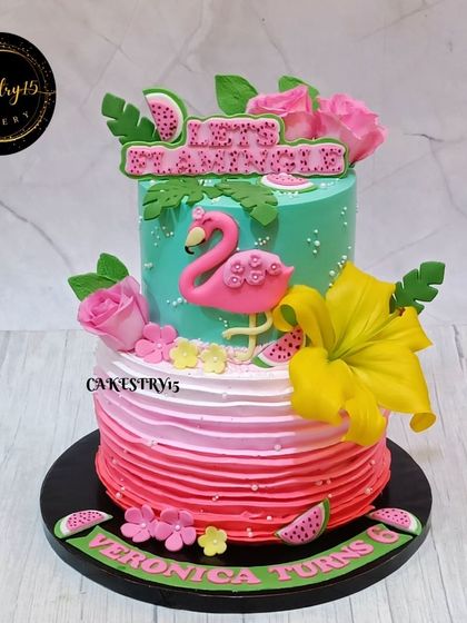 A tropical two-tier flamingo-themed cake for a 6th birthday. The cake features a pink ombre bottom tier and a turquoise top tier with a fondant flamingo and watermelon slices.