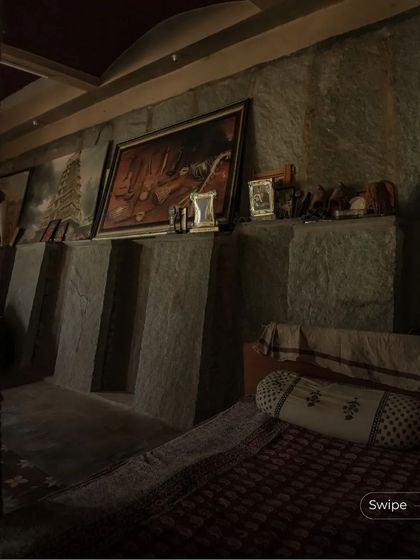 A moody and atmospheric bedroom in the Padmaja Rao Residence, with walls of exposed stone and a collection of traditional art.