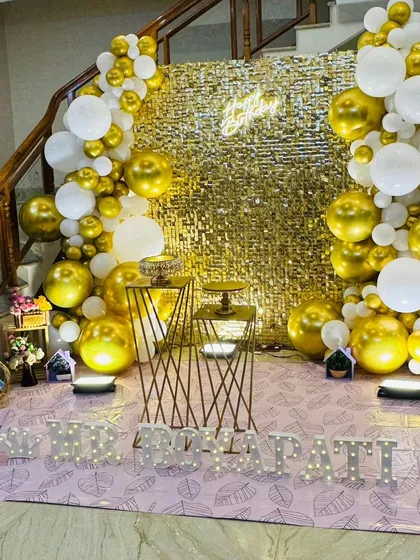 A classic and highly requested setup for birthdays and anniversaries. This features a gold sequin wall, a white and gold organic balloon arch, and custom marquee letters, all brought together with warm uplighting for a celebratory feel.