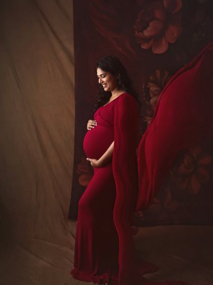 A classic side profile portrait, beautifully showcasing the baby bump. The flowing red fabric adds a touch of drama and elegance to this timeless maternity shot.
