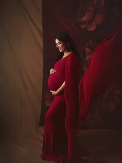 A classic side profile portrait, beautifully showcasing the baby bump. The flowing red fabric adds a touch of drama and elegance to this timeless maternity shot.