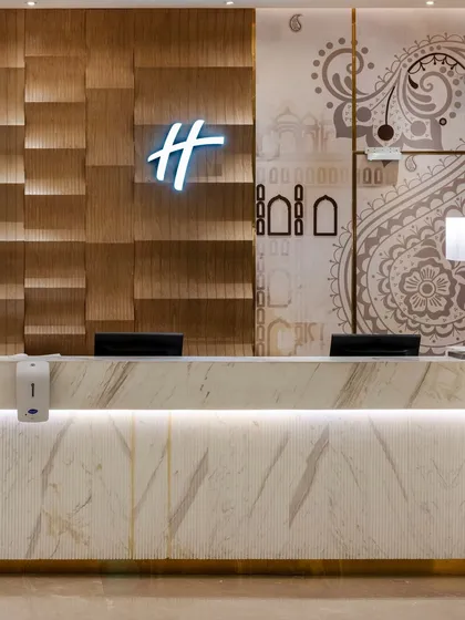 A close-up of the reception desk at Holiday Inn, Lucknow, where we integrated local heritage into the design. The backdrop features a textured wood panel and a subtle wall graphic inspired by Lucknow's architecture, set against a sleek, illuminated Italian marble desk.