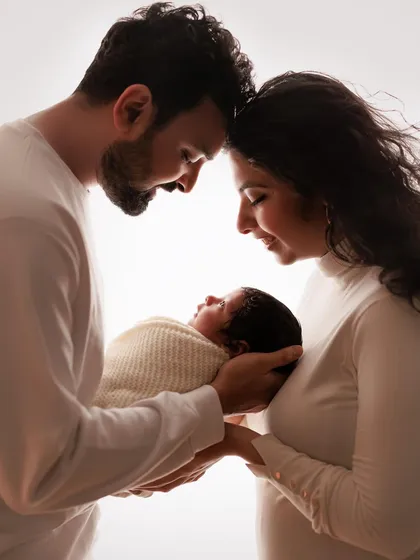 The embrace of parenthood. This backlit silhouette beautifully captures the intimate bond and shared love between new parents as they hold their baby.