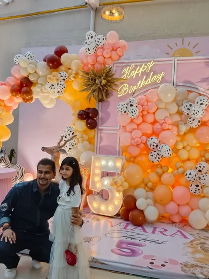 A whimsical animal-themed party with a pastel color scheme and dalmatian-print balloons. The setup includes a light-up number '5' and a neon 'Happy Birthday' sign.