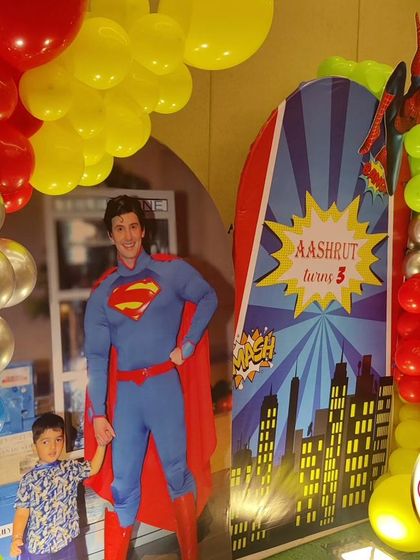 A superhero-themed third birthday with a life-sized Superman cutout. The decor also features Spider-Man and a city skyline backdrop.