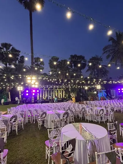 An outdoor reception setup at dusk with purple uplighting. The combination of string lights, elegant table settings, and ambient lighting creates a sophisticated and magical atmosphere.