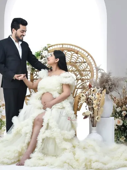 A tender moment between a couple during their maternity session. The father-to-be gently touches his partner's hair as she sits in a beautiful cream-colored gown.