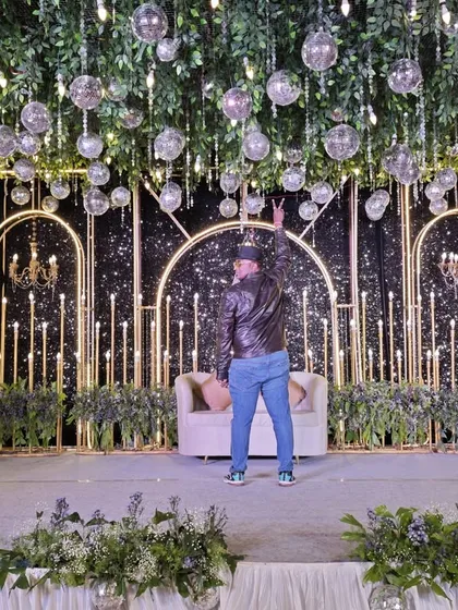 A glamorous sangeet stage setup featuring a ceiling of hanging greenery and disco balls. The dark, starry backdrop and elegant chandeliers add a touch of vintage disco, perfect for a night of music and dancing.