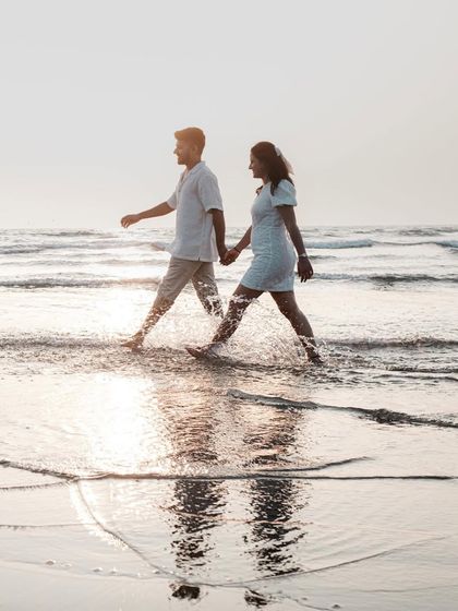 A beautiful shot of the couple walking through the shallow waves, their reflections trailing behind them. It's a serene and romantic moment.