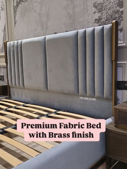 A closer look at this premium fabric bed. The headboard has elegant vertical pleating, and the solid wood frame is finished with subtle brass accents for a touch of luxury.