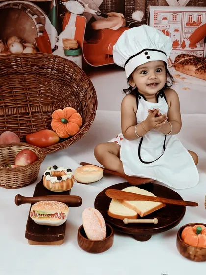 Our little master chef is ready to get cooking! This toddler is all smiles, surrounded by a delightful mess of toy food and kitchen props in our chef-themed studio setup.