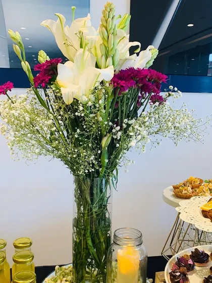 A close-up of a fresh flower centerpiece featuring white lilies, purple carnations, and baby's breath. These arrangements are perfect for adding a touch of natural beauty to any event space.