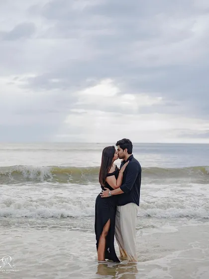 An intimate kiss with the vast ocean behind them. This photo captures a classic romantic moment, made more dramatic by the cloudy sky and rolling waves of the Goa beach.