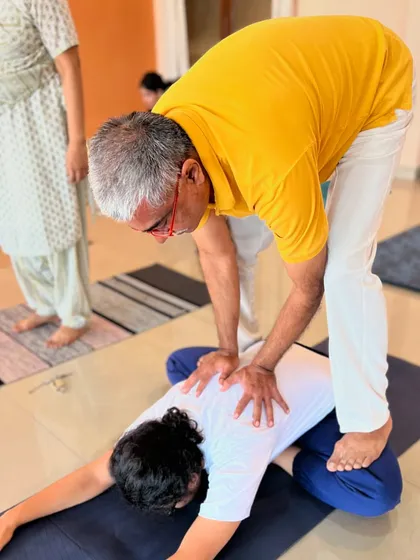A teacher provides a gentle adjustment in a forward bend, demonstrating the care and expertise we bring to every class.
