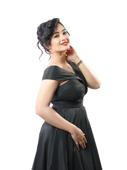 A full portrait of actress Girija Prabhu. Her simple black dress is elevated with a classic makeup look, featuring a red lip and an elegant updo for a timeless and sophisticated feel.