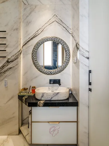 The vanity area is a focal point, with a black granite countertop, a unique marble basin, and an ornate, patterned round mirror that adds a touch of bespoke artistry.