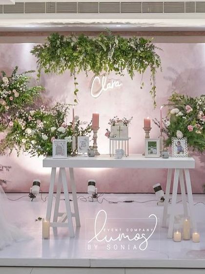 A beautiful baptism stage decorated in soft mauve and white. The elegant floral arrangements, tulle-draped table, and personalized name sign create a graceful and serene setting.