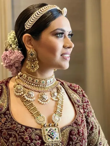A real bride with a classic low bun, adorned with pink and white flowers. The hairstyle is complemented by a traditional matha patti, creating a regal bridal look.