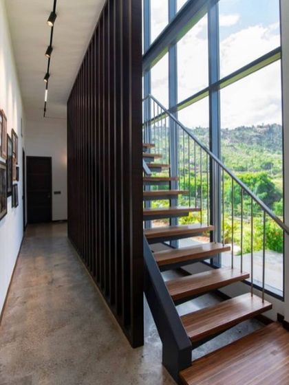 This is a duplicate of ID 72. A minimalist staircase with wooden treads runs alongside a double-height window, ensuring the connection to the lush exterior landscape is never lost.