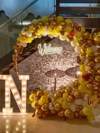 An elegant welcome party setup. I used a crescent-shaped balloon arch in gold and white, a 'Welcome' neon sign, and large marquee letters for the baby's initials.