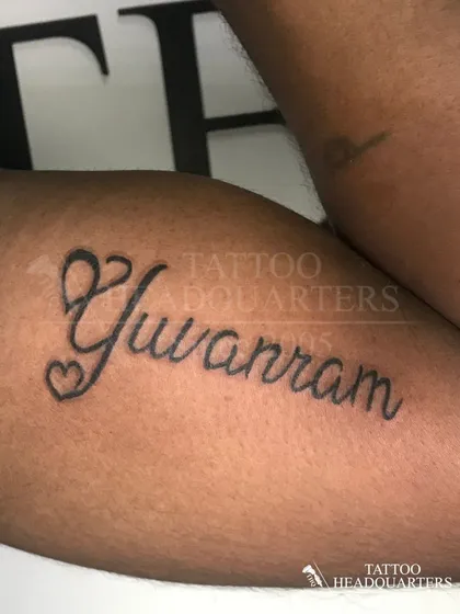 The name "Yuvram" in a flowing script with heart details, a beautiful and personal piece on the arm.