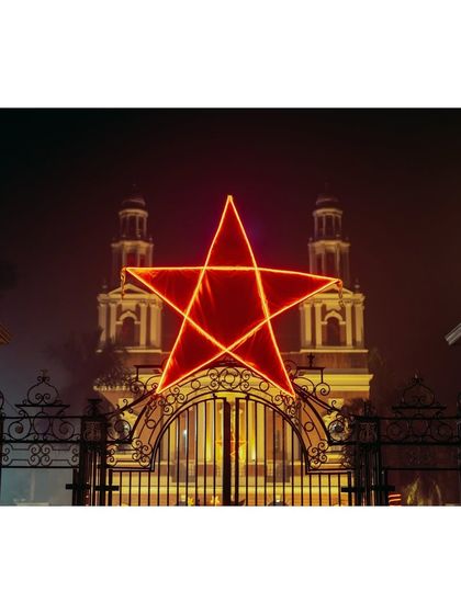 A giant, illuminated red star hangs over the entrance to the Sacred Heart Cathedral in New Delhi during Christmas. The foggy night and warm lights create a magical and festive atmosphere.