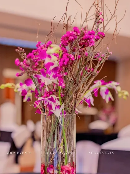 A tall centerpiece with vibrant pink orchids and rustic twigs in a clear glass vase. This arrangement adds height and a splash of color to event tables, suitable for a variety of corporate themes.