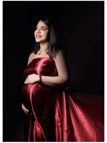 A radiant mother-to-be wrapped in a rich, red satin fabric. This minimalist setup with dramatic lighting creates a powerful and elegant maternity portrait.