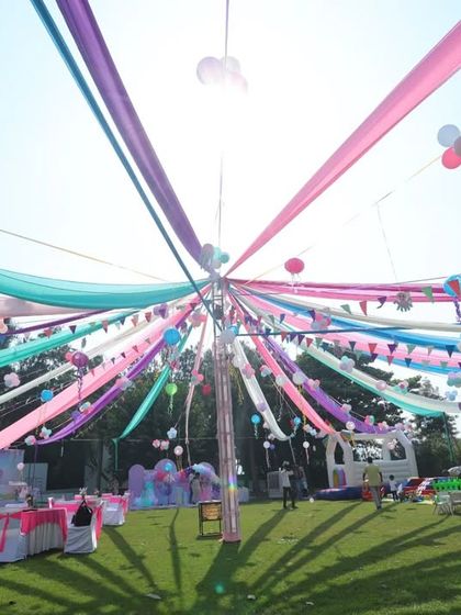 A wide shot of the beautiful outdoor setup for a birthday party, with colorful drapes creating a festive canopy. This shows the scale and effort put into the celebration.