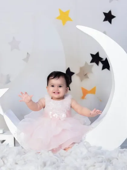 A one-year-old girl in a lovely pink dress sits on our moon prop, surrounded by stars. A magical way to celebrate turning one.