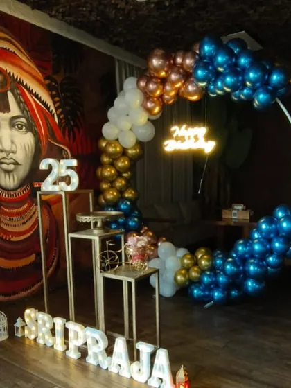 This birthday decor at a restaurant features a unique color palette of metallic blue, bronze, and gold balloons, along with light-up marquee letters for the name and age.