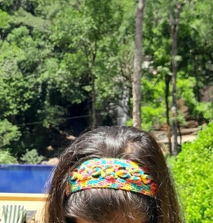 Here is another view of the crochet headband being worn outdoors. The natural light highlights the texture and bright colors of the yarn and the detailed flower pattern.
