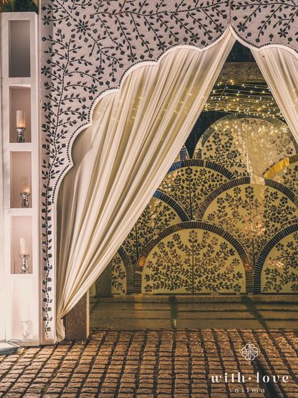 A peek through a draped archway reveals the intricate patterns of the Thikri mosaic wall. This layering of textures, from soft fabric to reflective mirror, creates depth and visual interest at the entrance of the event.