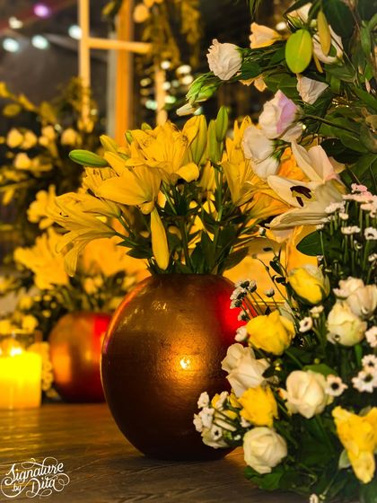 A close-up of the floral arrangements, showing a mix of yellow and white lilies and roses in metallic vases, with the soft flicker of candlelight creating a warm, romantic ambiance.