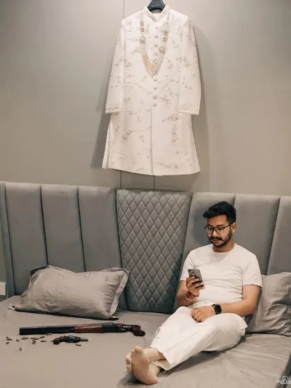 A candid, behind-the-scenes shot of the groom relaxing before the ceremony, with his sherwani hanging in the background, ready for the big moment.