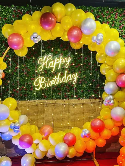 A vibrant yellow and red balloon ring backdrop against a green wall for Yash's first birthday celebration.