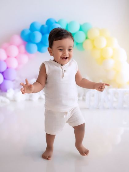 Dancing into year one! This happy toddler is celebrating his first birthday with a colorful rainbow balloon backdrop.