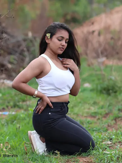 A simple and natural outdoor portrait of a model in a white tank top and black jeans. The kneeling pose in a grassy field feels relaxed and authentic.