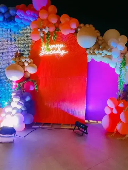 A bold and colorful rooftop party for a 35th birthday. The backdrop combines a red panel with a silver sequin wall, framed by a multi-colored balloon garland and large marquee numbers.