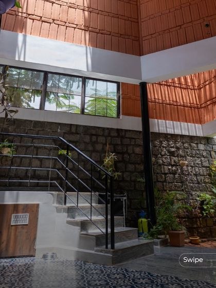 The interior of the Gifty Residence, showing the interplay of the stone wall, terracotta accents, and the open staircase under a skylight.