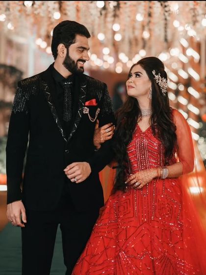 A perfect couple's look for a reception or engagement. The groom wears our custom black suit with unique silver embroidery on the shoulders and lapels, complementing his partner's vibrant red gown.