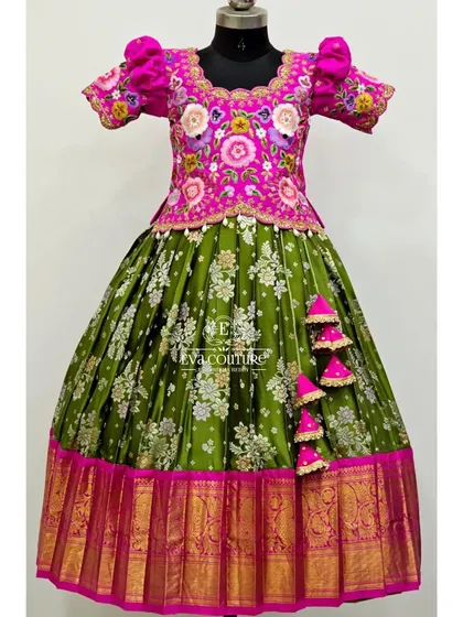 A grand-looking lehenga with a heavily embroidered pink blouse and a floral brocade skirt in olive green. The puff sleeves and latkans add a playful touch.