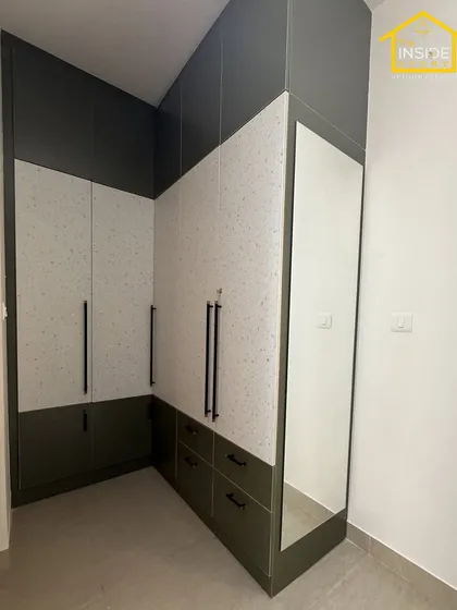 We designed this L-shaped wardrobe to maximize storage in the corner of the bedroom. The combination of dark green and speckled white laminate, along with a full-length mirror, adds style and practicality.