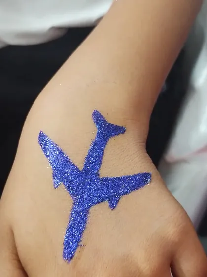 A solid blue glitter airplane tattoo on the hand. This is a fun and simple design for kids who love transportation themes.