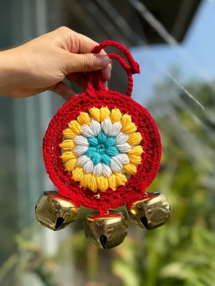 A red ghungroo hanging with a central floral motif in yellow, white, and blue. A very traditional and vibrant design.