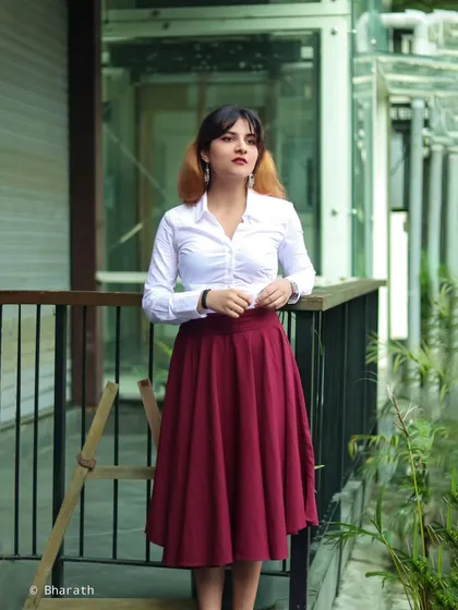 An outdoor portrait of a model in a classic white shirt and a flowing maroon skirt. The setting on a modern balcony adds a clean, architectural element.