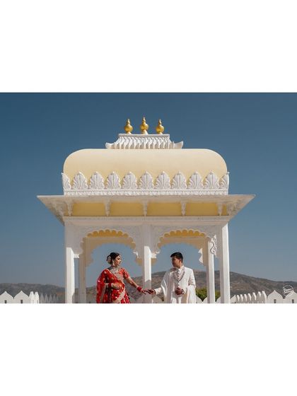 A couple shares a promise under a traditional Rajasthani cenotaph against a clear blue sky. This minimalist yet grand composition from their Udaipur wedding is both elegant and powerful.