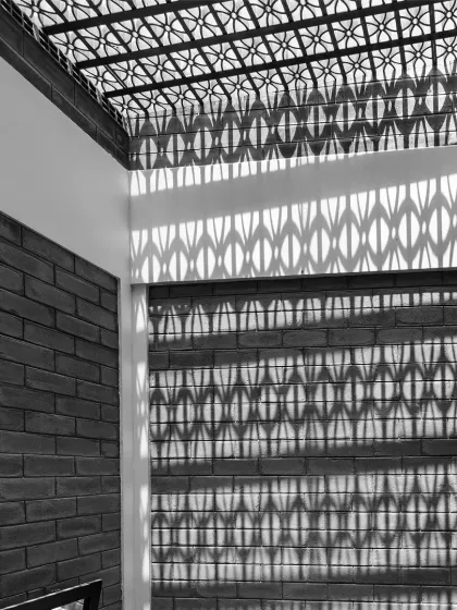 We use architecture to paint with light. Here, a patterned jaali skylight casts intricate shadows on an exposed brick wall, a dynamic display that changes with the sun's journey across the sky. This is how we create spaces that feel active and ever-changing, without using any energy.